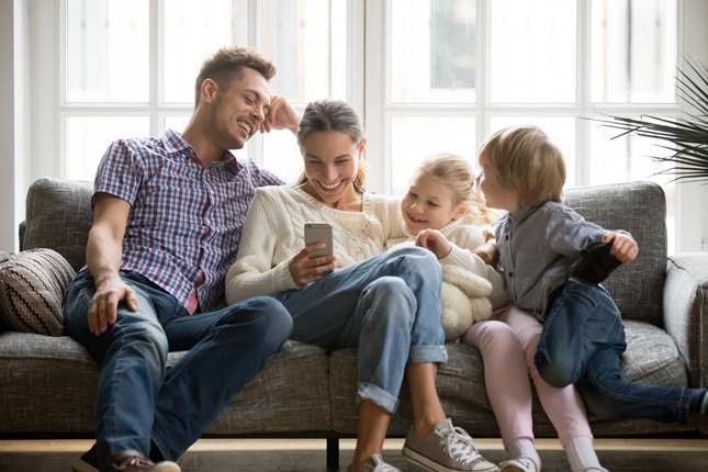 A family of four sitting on a sofa watching content on a smartphone.