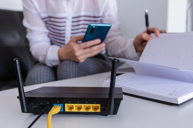 A consumer checking their phone and writing down instructions next to the internet router.